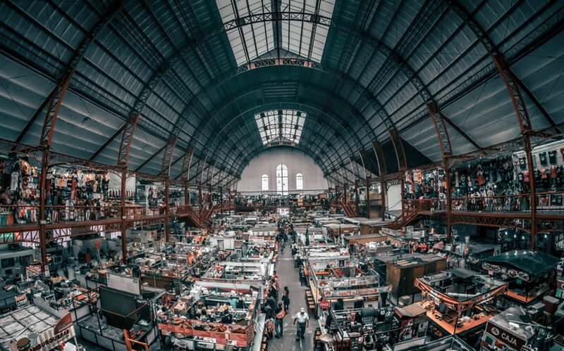 A bustling indoor market with a high arched ceiling and many stalls.