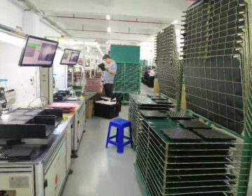 Factory worker inspecting electronic components on shelves.