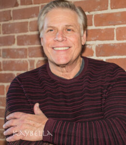 Smiling man in striped sweater, brick background.